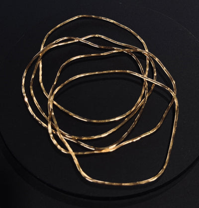 A group of five gold metal bangle bracelets with a hammered or textured finish, displayed on a dark surface.
